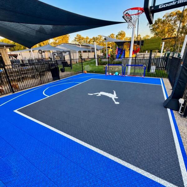 Slam Man basketball court kit installed under shade sail in Logan Village with blue outer court tiles